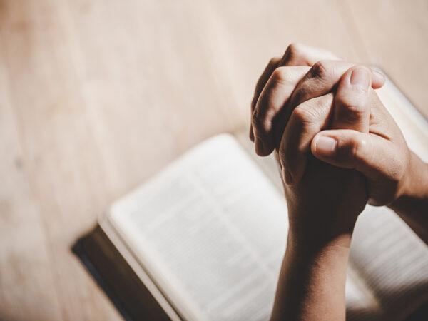 Espiritualidade e religião, mãos postas em oração sobre uma Bíblia Sagrada.